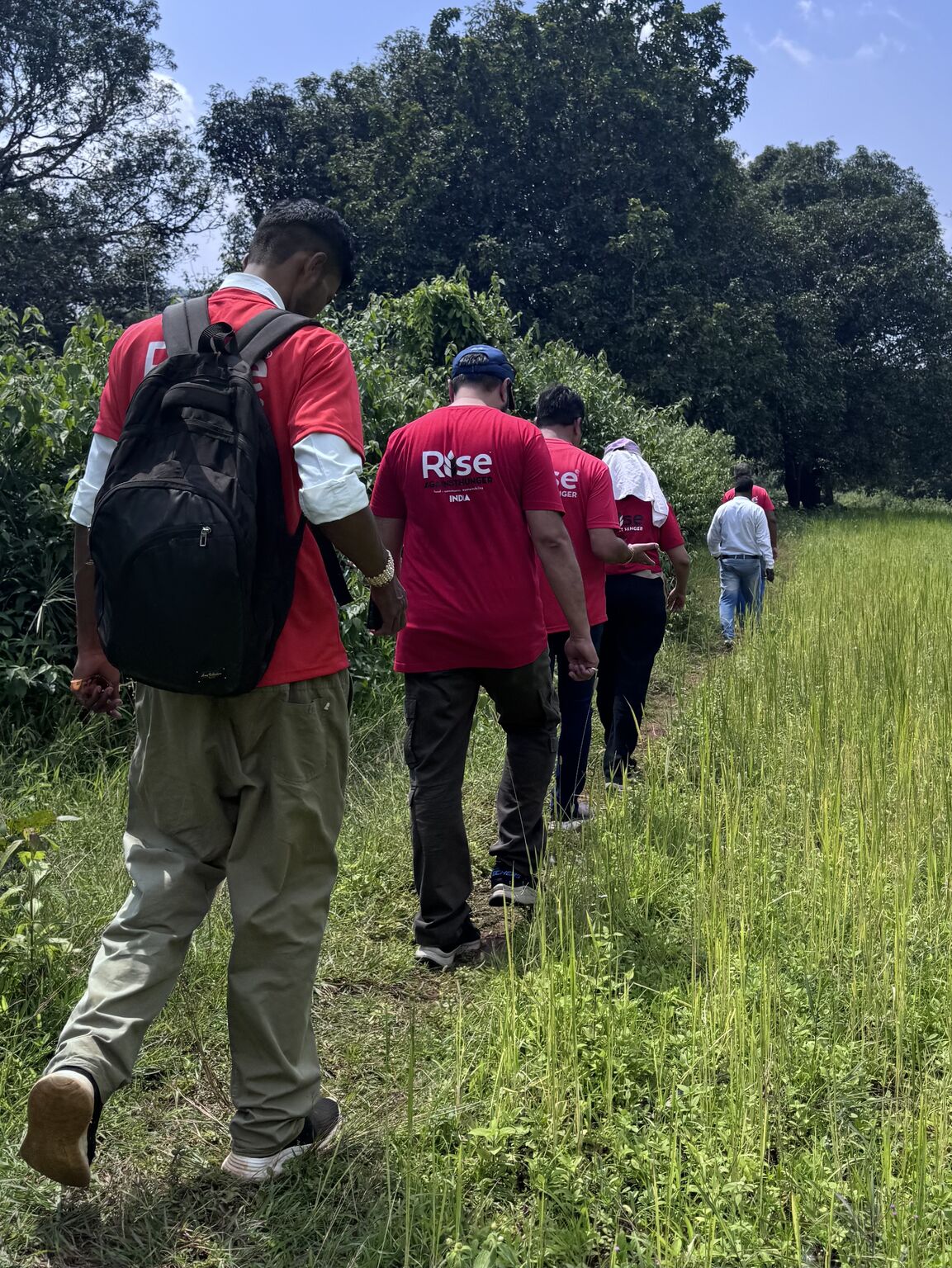 The RAHI team trekking single-file through a grassy rural path to reach remote villages in Dantewada